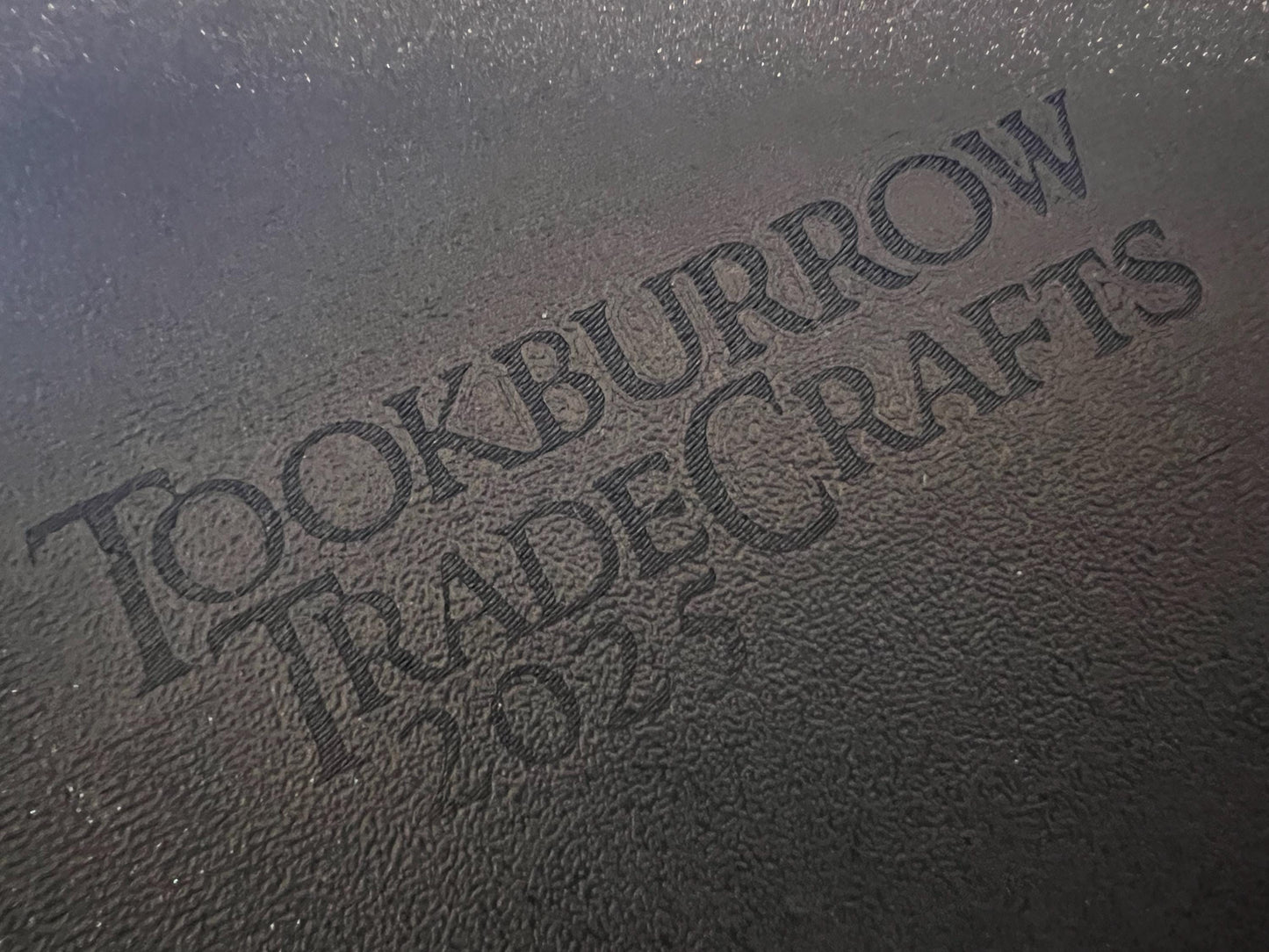 Close-up of textured black surface with engraved Tookburrow TradeCrafts 2024 logo on matte material