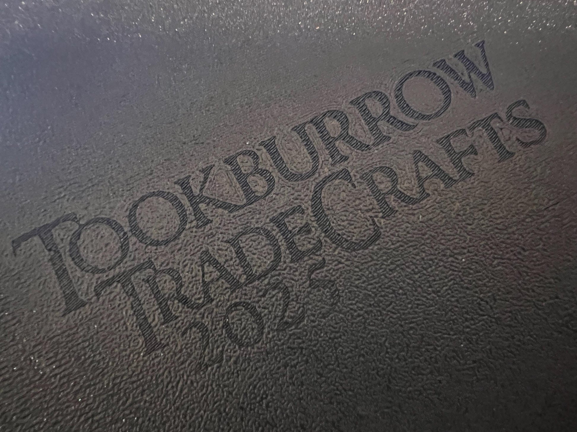 Close-up of textured black surface with engraved Tookburrow TradeCrafts 2024 logo on matte material