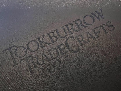 Close-up of textured black surface with engraved Tookburrow TradeCrafts 2024 logo on matte material